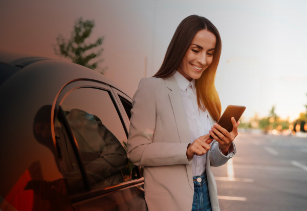 Immagine che rappresenta una donna sorridente appoggiata ad un'auto che guarda il suo smartphone