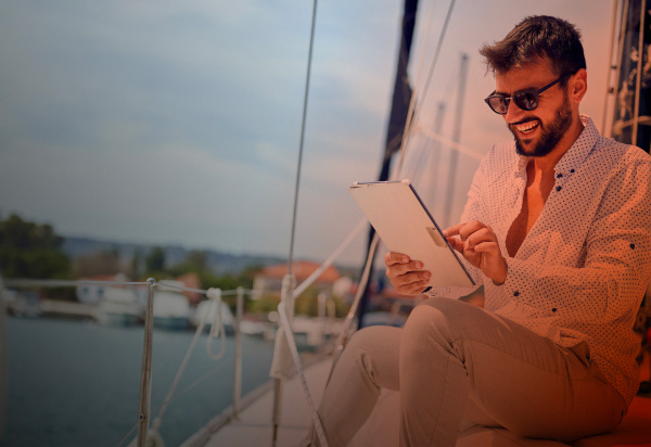 Immagine che rappresenta un ragazzo sorridente seduto in barca mentre guarda il suo tablet